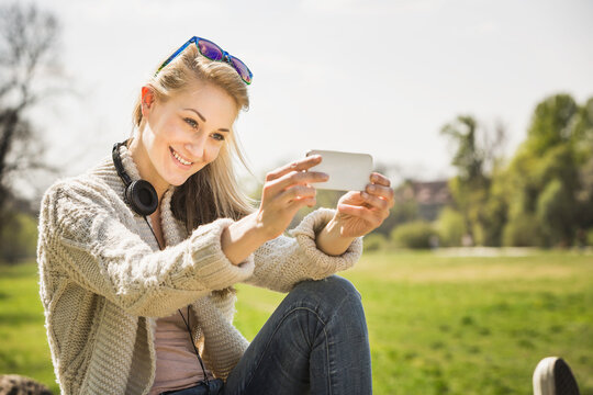 Young woman spending time in the spring sunny weather, taking selfies and listening to music. Munich, Germany