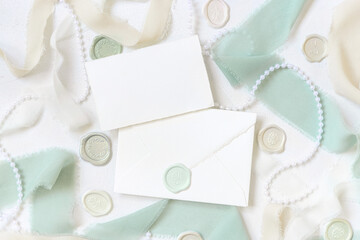 Card and envelope near light green and beige decorations and silk ribbons on white table top view,...