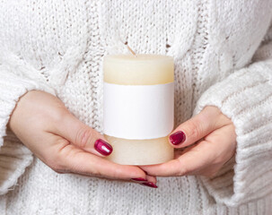 Woman in white sweater with cream candle with blank label in hands, mock up