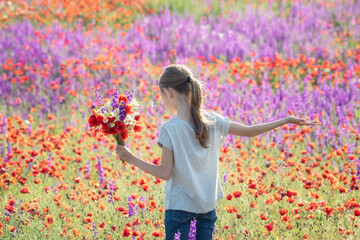 Beautiul caucasian girl holding big bouquet with poppies on the background of a colorful spring field.