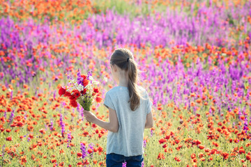 Beautiul caucasian girl holding big bouquet with poppies on the background of a colorful spring...