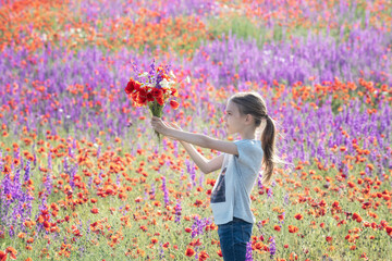 Beautiul caucasian girl holding big bouquet with poppies on the background of a colorful spring field.