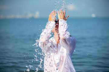 A woman in a white wet shirt is bathing and doused with sea water.