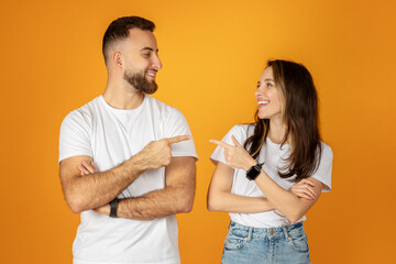 A young man and woman, both wearing white t-shirts and smiling, playfully point at each other