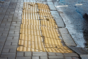 Dented yellow tactile tiles on sidewalk in front of pedestrian crossing. Damaged warning tiles for...