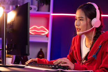 Host channel of beautiful Asian girl streamer concentrating online game wearing headphones pastel color talking with viewers media online. Esport skilled team players in neon blue room. Stratagem.