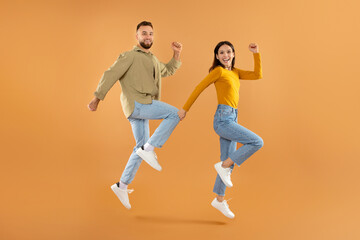 Fototapeta na wymiar couple jumping shaking their clenched fists in celebration, orange background