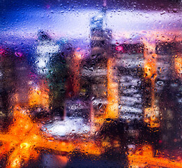 View through a glass window with raindrops on city streets with cars in the rain, bokeh of colorful...