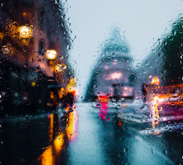 Obraz na płótnie Canvas View through a glass window with raindrops on city streets with cars in the rain, bokeh of colorful city lights, night street scene. Focus on raindrops on glass 
