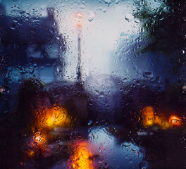 Obraz na płótnie Canvas View through a glass window with raindrops on city streets with cars in the rain, bokeh of colorful city lights, night street scene. Focus on raindrops on glass 