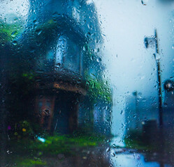 view through glass covered with raindrops onto the street of a small European town covered in morning fog. focus on raindrops	