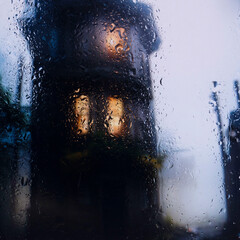 view through glass covered with raindrops onto the street of a small European town covered in...