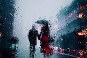 View through glass window with rain drops on blurred reflection silhouettesof a man and girl in...