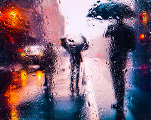 View through a glass window with raindrops on city streets with cars in the rain, bokeh of colorful city lights, night street scene. Focus on raindrops on glass