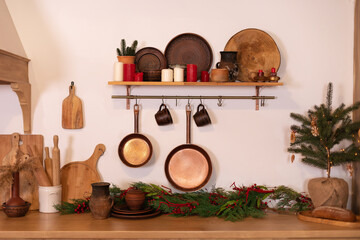 Interior scandi cuisine. Wooden shelf with various clay cookware and decoration in the kitchen. Different kind of cookware and tools on tabletop. Kitchen Railing on wall with coppers skillets and cups