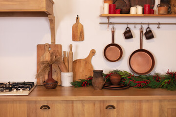 Interior scandi cuisine. Wooden shelf with various clay cookware and decoration in the kitchen. Different kind of cookware and tools on tabletop. Kitchen Railing on wall with coppers skillets and cups