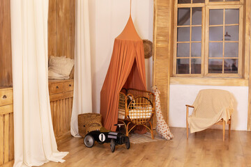 Rustic playroom interior with rattan crib with canopy, wicker baskets, toys and window. Wickered cradle bed with baldachin in newborn room in scandi style at home. Black racing car toy in a child room © stock_studio