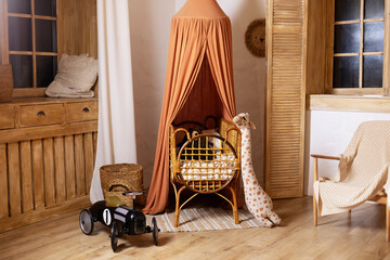 Rustic playroom interior with rattan crib with canopy, wicker baskets, toys and window. Wickered cradle bed with baldachin in newborn room in scandi style at home. Black racing car toy in a child room © stock_studio