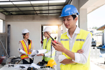 Portrait of a male engineer at a construction site using a walkie-talkie. Standing in charge of planning a construction project in formal attire, wearing a hard hat, a successful civil engineer.