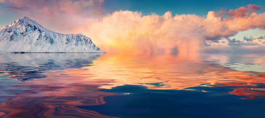 Huge snowy peak reflected in the calm waters of Norwegian sea. Caolorful sunrise on Lofoten...