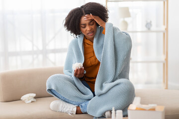 Distressed young woman with curly hair sitting on a couch, wrapped in a blue blanket