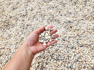 A woman uses her left hand to scoop  pebbles from the playground's gravel pit. Small colorful round stones are commonly used to decorate gardens. Granite gravel stone rocks flooring pattern surface

