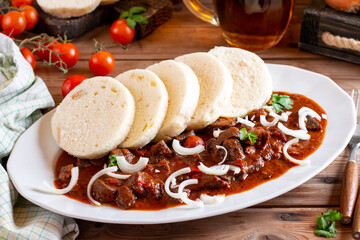 Traditional Czech Goulash meal with dumplings on plate on wood table, beer.