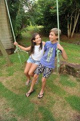 Fototapeta premium irmãos brincando em balanço no parque , férias escolares 