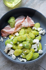 Potato gnocchi served with green pea sauce, feta cheese and bacon in a grey bowl, middle closeup, vertical shot