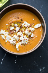 Sweet potato soup topped with feta cheese and chopped pistachios, vertical shot on a black marble surface, elevated view, middle closeup