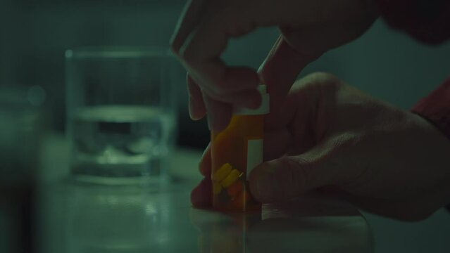 Container for tablets. An unhealthy man dressed in loungewear takes pills from an orange bottle. Close-up of a young man being treated with pills, treated with modern drugs, medicine