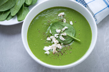 Spinach cream-soup topped with feta cheese and served in a white bowl, horizontal shot on a grey...