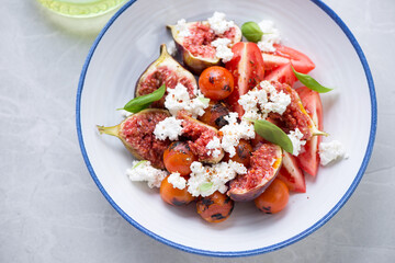Salad with tomatoes, fresh figs, goat cheese and green basil served in a blue and white plate, horizontal shot