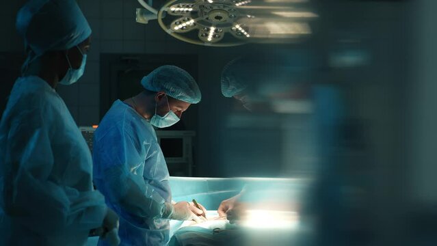 Professional cooperating team of multiethnic surgeons performing organ transplant operation surgery in modern dark operating room. Concept of surgery and emergency. Shooting in slow motion.