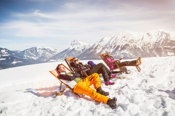 Group of friends lying in a lounge chairs sleeping in the mountains in winter. Achenkirch, Austria