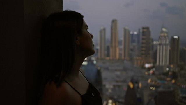 Silhouetted woman gazes contemplatively at the dubai skyline during twilight from a high view observatory.