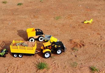 Plastic toy cars, tractor and dump trucks on the sand in the park
