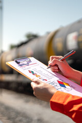 Action of an engineer is checking on chemical hazardous material checklist form with background of train freight tanker for crude oil or chemical cargo. Industrial safety working scene. 