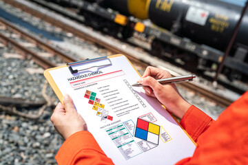 Action of an engineer is checking on chemical hazardous material checklist form with background of train freight tanker for crude oil or chemical cargo. Industrial safety working scene.  - obrazy, fototapety, plakaty