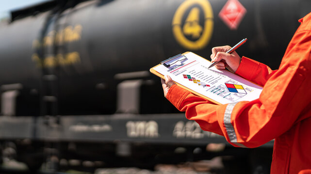 Action of an engineer is checking on chemical hazardous material checklist form with background of train freight tanker for crude oil or chemical cargo. Industrial safety working scene. 