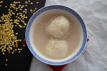A bowl of homemade glutinous rice ball dessert with coconut milk and sesame seeds.