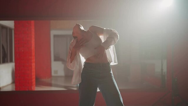 Young attractive woman is dancing hip hop contemporary in dace hall close-up on white light. Shooting of modern slow dance choreography. Motion of female dancer expressing feelings in dance movings. 
