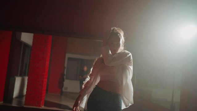 Young attractive woman is dancing hip hop contemporary in dace hall close-up on white light. Shooting of modern slow dance choreography. Motion of female dancer expressing feelings in dance movings. 