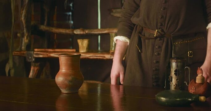 Bartender leans on counter in medieval tavern. Attentive barkeeper in brown dress listens to guest order in store. Visiting ancient bar adventure