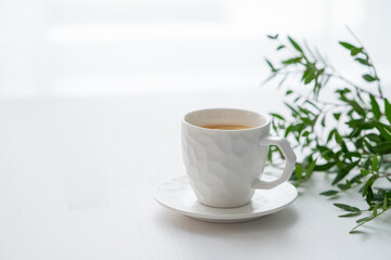 A cup of tea with lemon and green branch on a white table against the background of a kitchen...