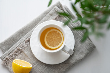 A cup of tea with lemon, napkin and green branch on a white table.