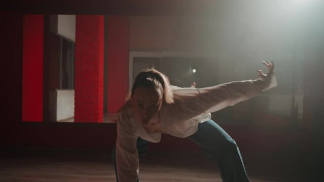 Young attractive woman is dancing hip hop contemporary in dace hall close-up on white light. Shooting of modern slow dance choreography. Motion of female dancer expressing feelings in dance movings. 