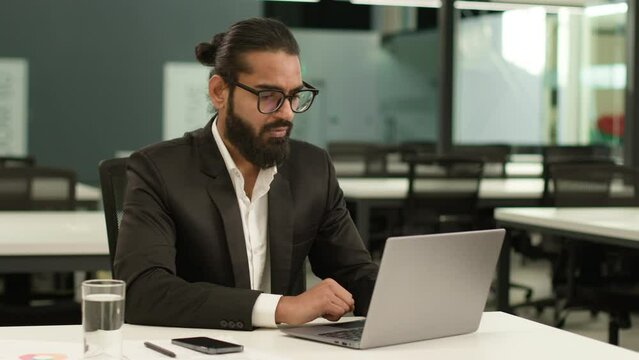 Busy concentrated Indian male employer company corporate Arabian entrepreneur boss CEO business man Muslim businessman at office with laptop working typing thinking solution idea pensive looking away