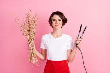 Photo portrait of cute hairdresser keeping hot hair straightener dry plants isolated pastel pink color background
