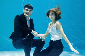 Artistic business concept. Man and woman shaking hands underwater on blue background